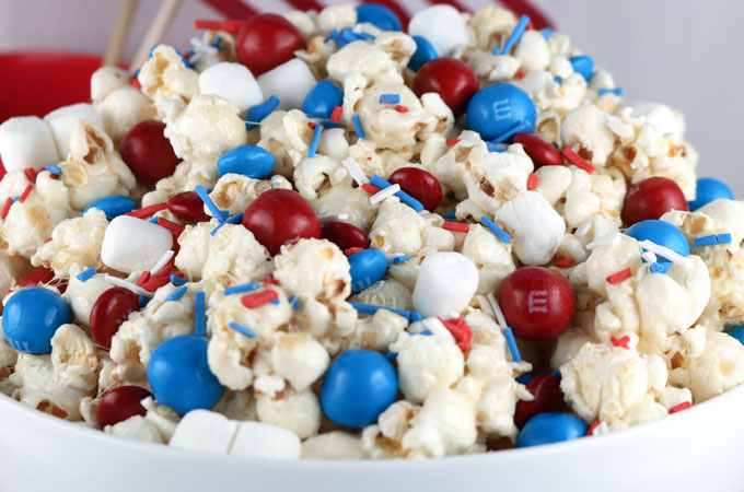 Celebrate with our Patriotic Popcorn - a fun 4th of July Dessert that is both sweet and salty and chock full of Red White and Blue Candy. This yummy Fourth of July treat is super delicious and so easy to make. It would be great at a 4th of July Party, a Memorial Day barbecue or an Olympics viewing party. Pin this yummy 4th of July snack for later and follow us for more great 4th of July Food Ideas.