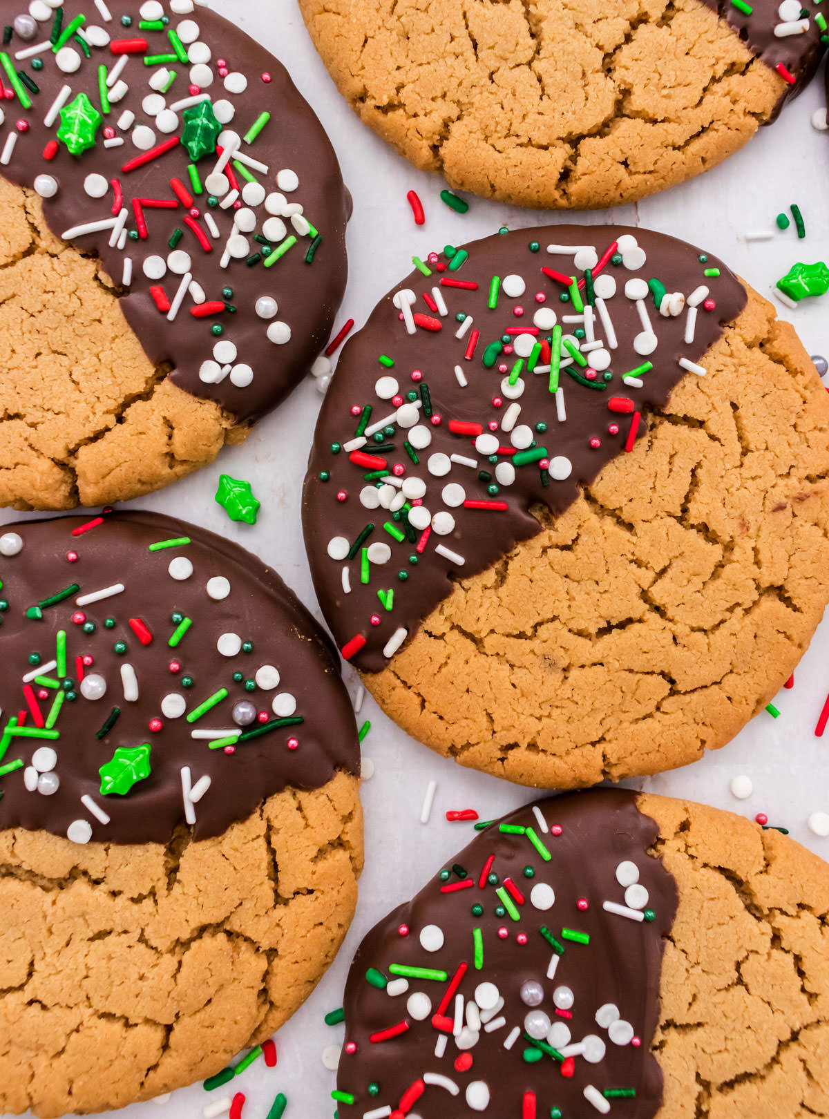 Closeup on five Chocolate Dipped Peanut Butter Cookies laying flat on white parchment paper surrounded by sprinkles.