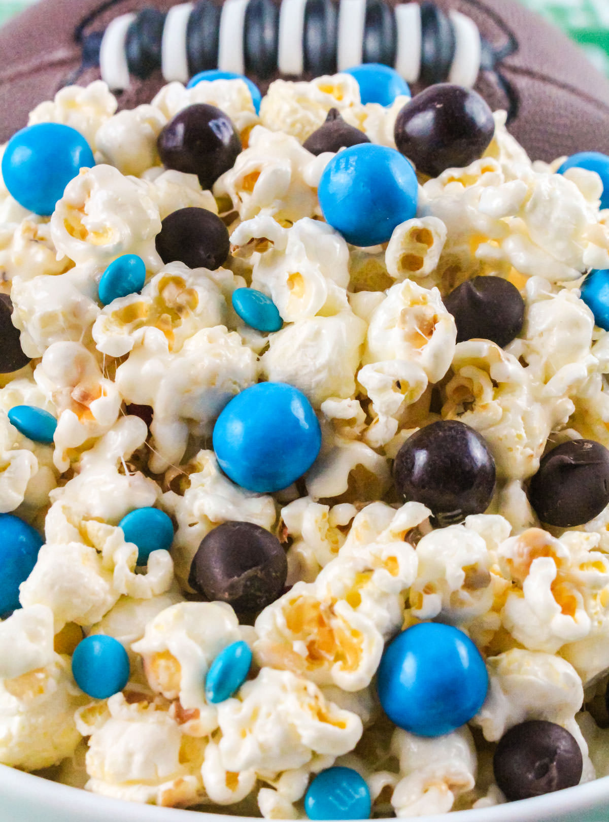 Closeup on on a white serving bowl filled with a batch of Carolina Panthers Popcorn sitting in front of a football.