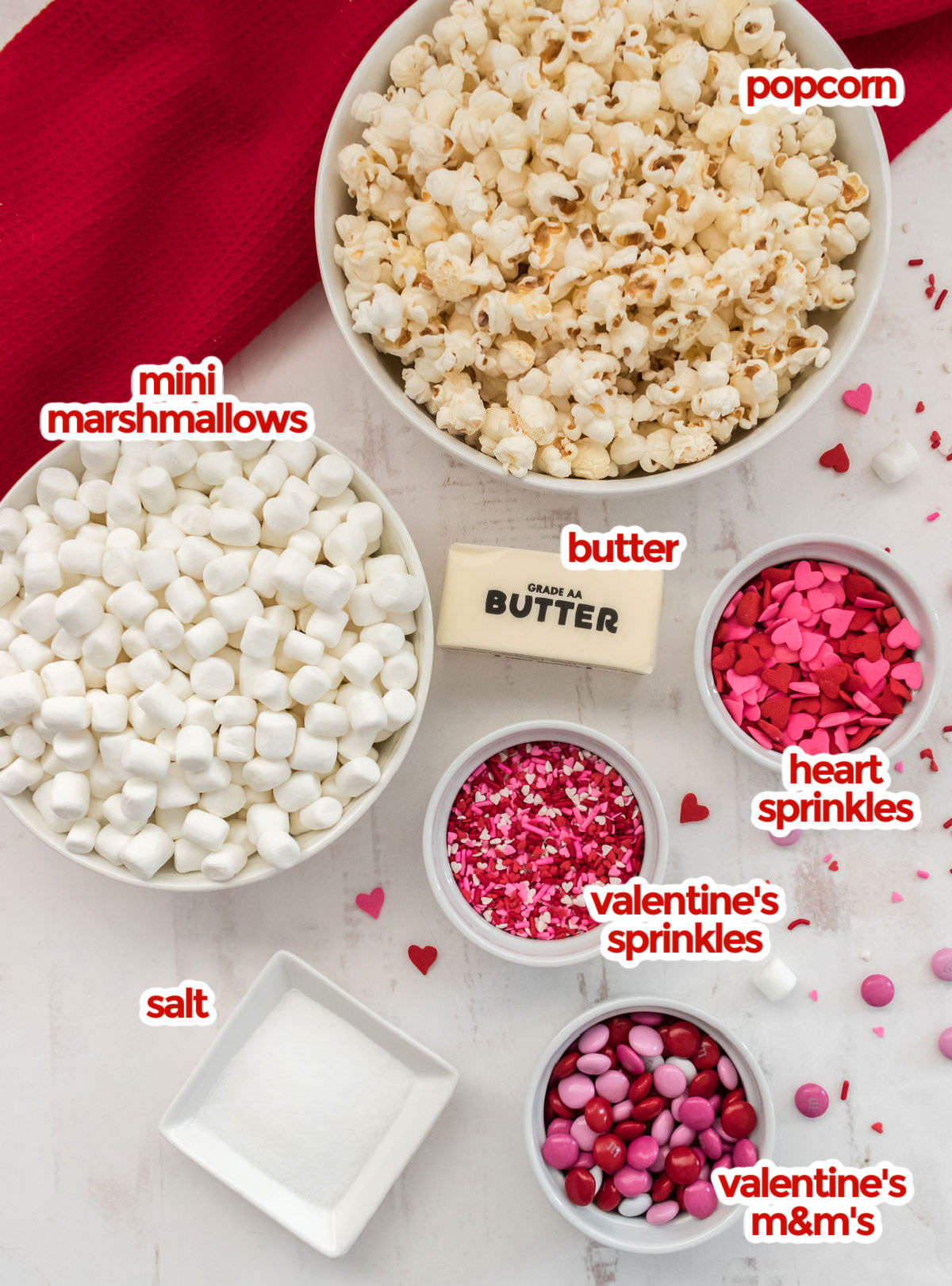 All the ingredients you will need to make Valentine's Day Popcorn including popcorn, marshmallows, butter, salt, heart sprinkles, valentine's sprinkles and valentine's mix M&M's.