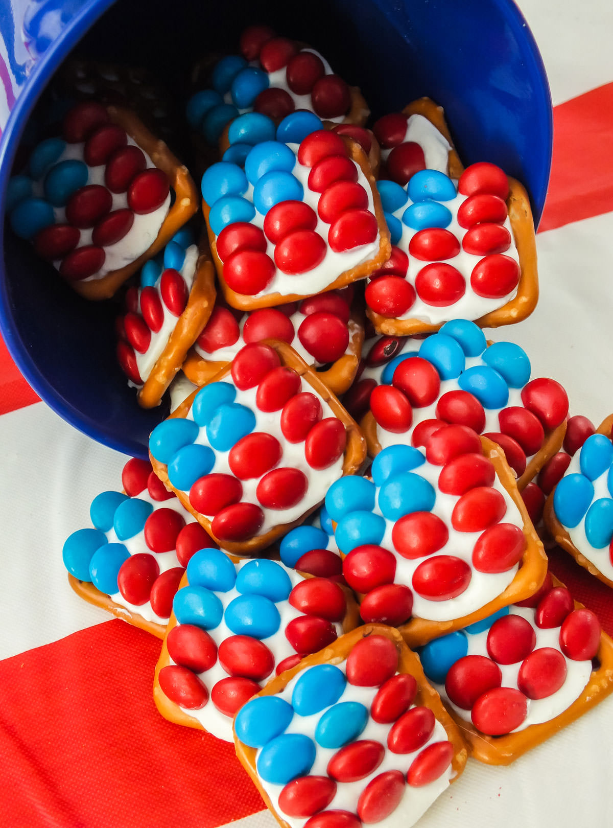 Closeup of Patriotic Pretzel Bites tumbling out of a blue pail onto an American flag table cloth.