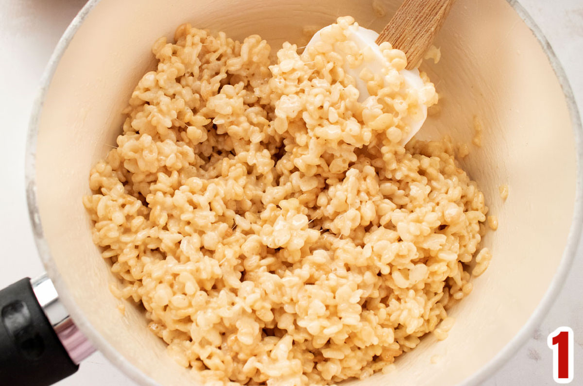 Closeup on a white pan filled with warm Rice Krispie Treat mixture and a white wooden spoon.
