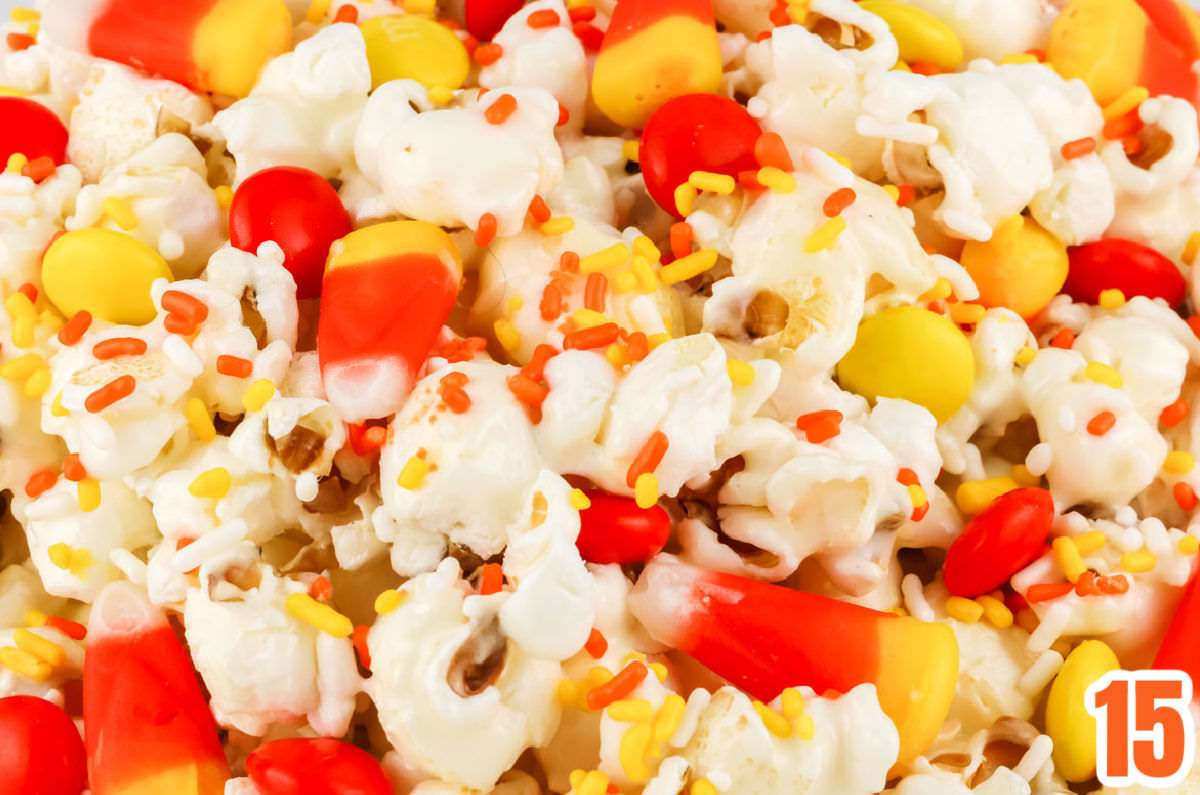 Closeup on a batch of Fall Candy Corn Popcorn highlighting the marshmallow popcorn, the candy corn, the yellow and orange M&M's and the sprinkles.