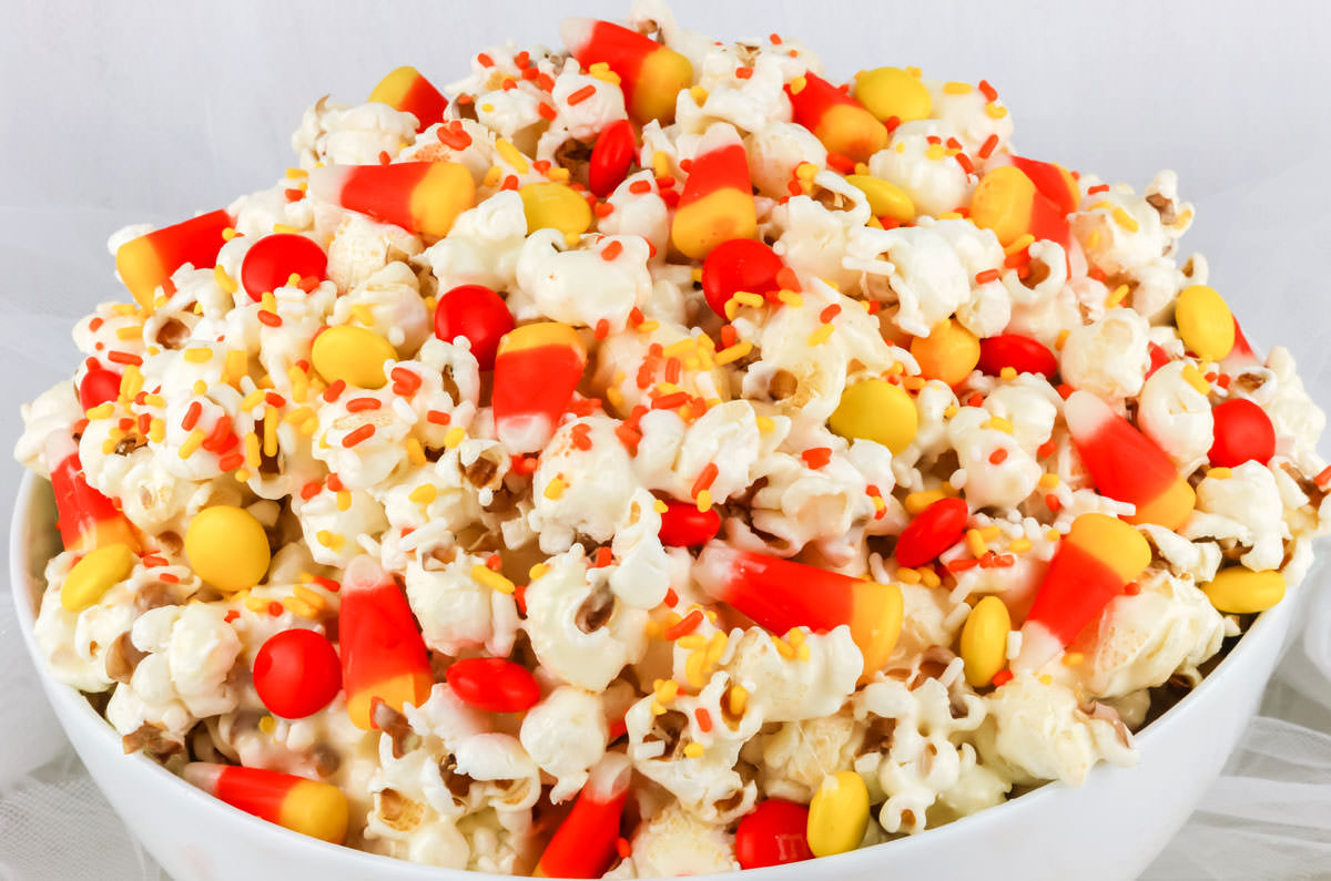 Closeup on a batch of Fall Candy Corn Popcorn in a white serving bowl sitting on a white surface.