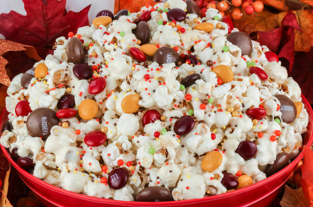Closeup on a red bowl filled with Fall Harvest Popcorn surrounded by Fall decorations.