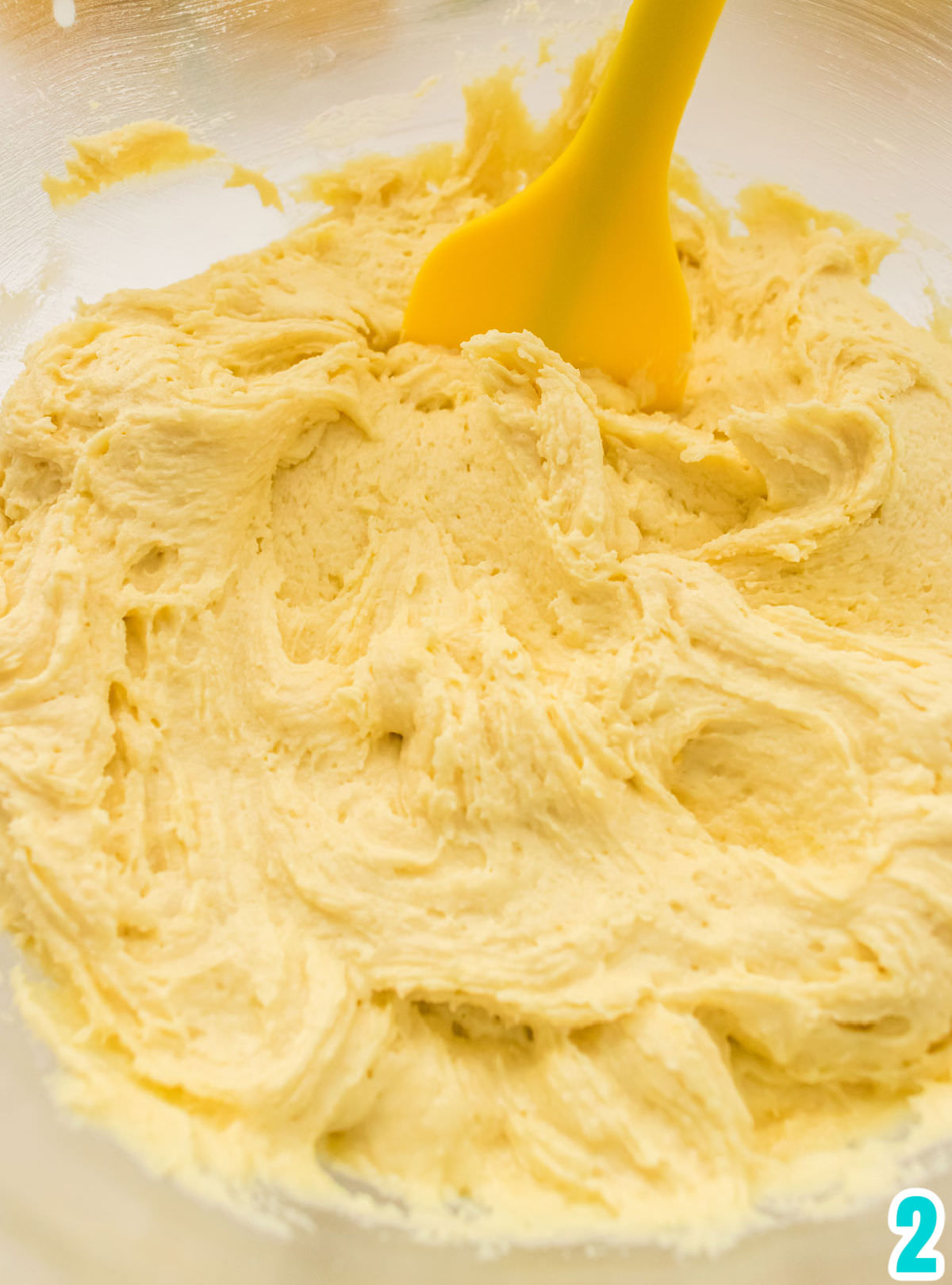 Closeup of a clear bowl filled with the Lemon Cookie dough and a yellow spatula.