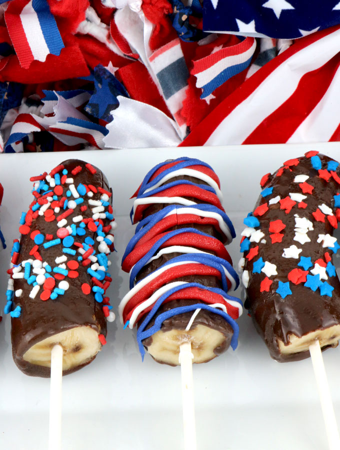 Red White and Blue Frozen Bananas - easy to make patriotic homemade chocolate covered frozen bananas for a 4th of July Party or a Memorial Day Barbecue. Call them Frozen Bananas or call them Monkey Tails but this delicious frozen summer treat will be a great 4th of July dessert. Pin this yummy Fourth of July treat for later and follow us for more 4th of July Food ideas.