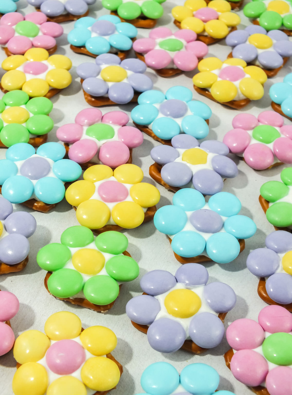 Close up on many Spring Flower Pretzel Bites spread out across a white surface.