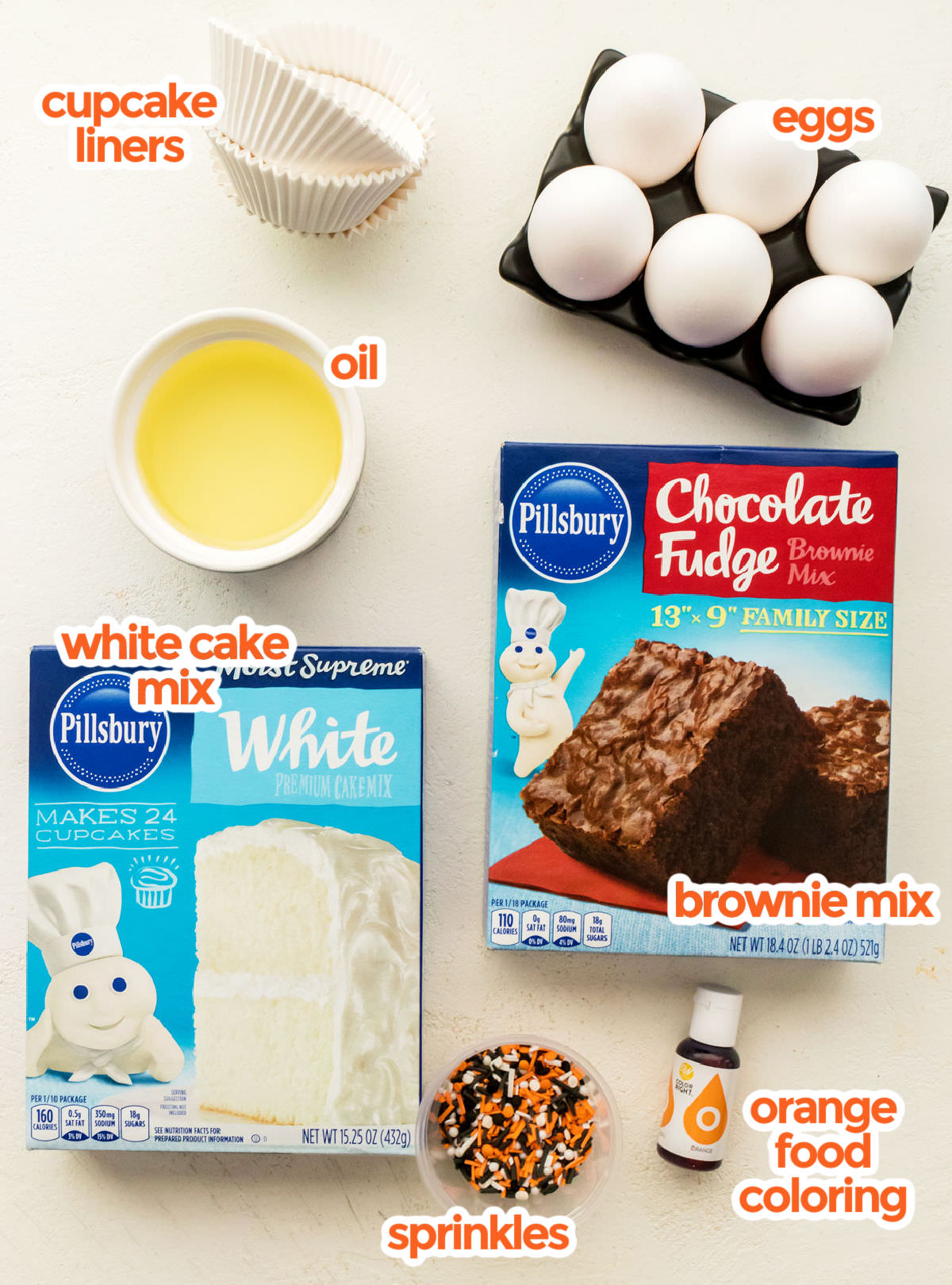 All the ingredients you will need to make Halloween Brownie Cupcakes including White Cake Mix, Brownie Mix, Eggs, Oil, Food Coloring and Halloween Sprinkles.
