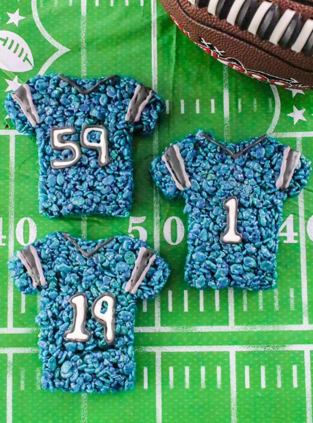 Three Carolina Panthers Rice Krispie Treats sitting on a football field tablecloth.